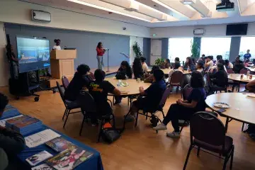 Students gather at round tables to engage in reading session.